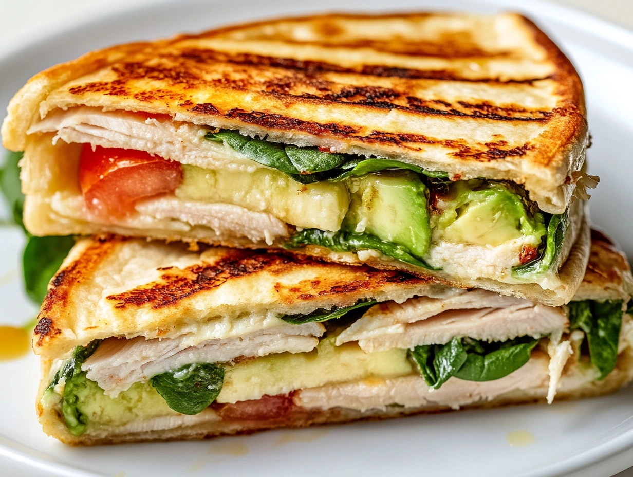 Close-up of a grilled tortilla wrap sliced in half, showing layers of spinach, tomato, avocado, turkey, and melted cheese.