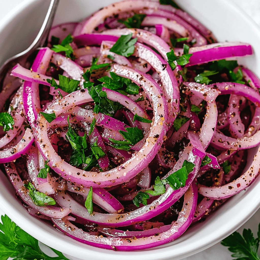 A colorful onion salad featuring thin red onion slices and parsley, seasoned with herbs and black pepper.
