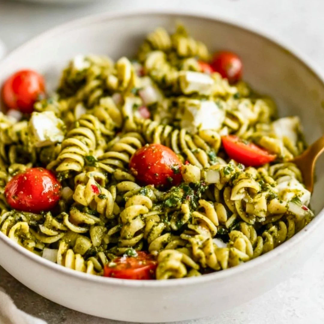 Pesto pasta salad with fresh vegetables and herbs in a bowl