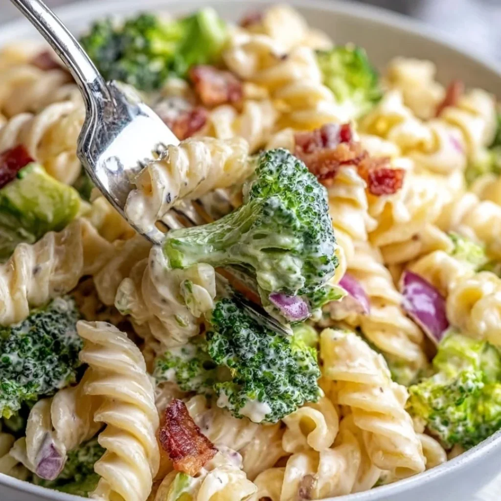 A bowl of colorful broccoli pasta salad with greens and dressing