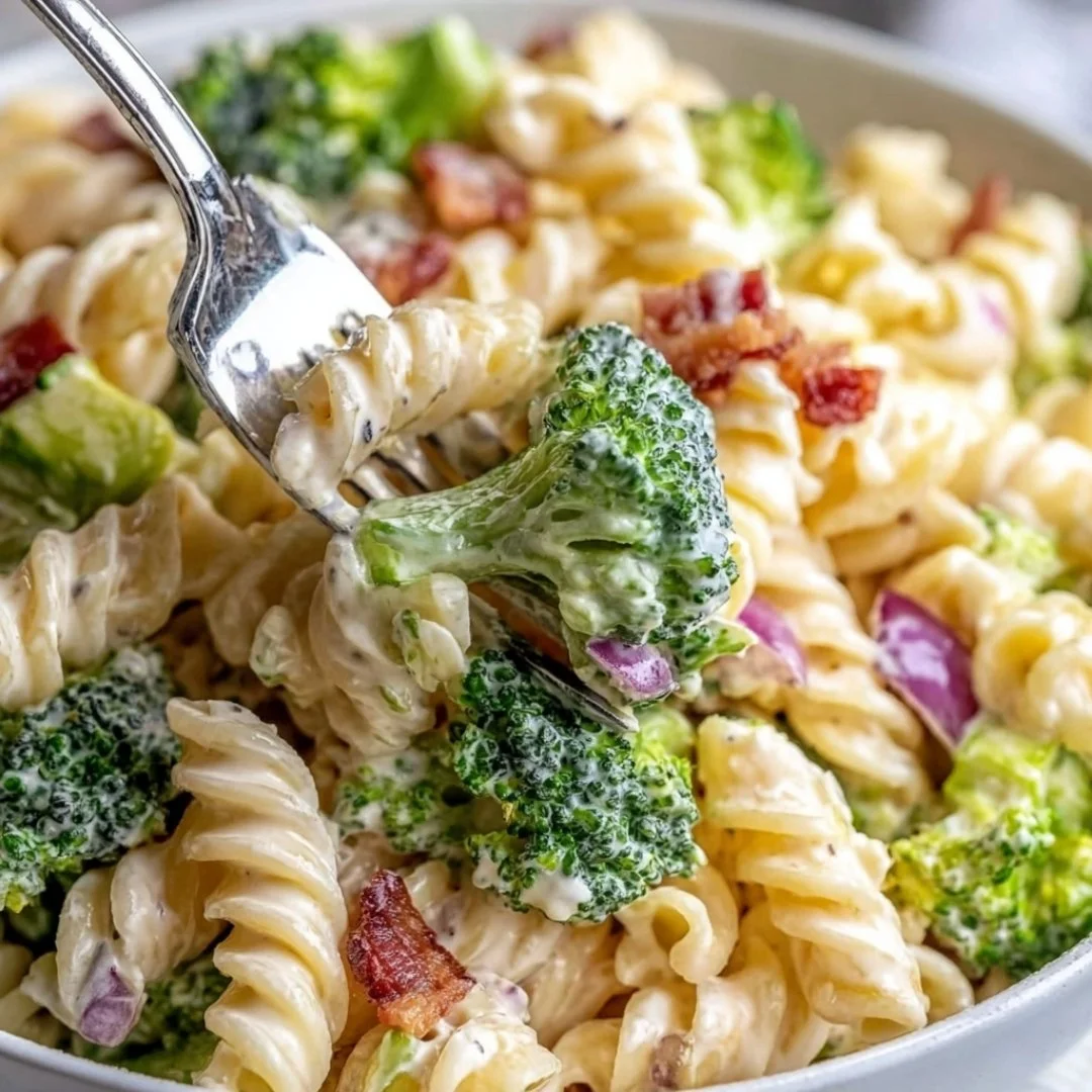 A bowl of colorful broccoli pasta salad with greens and dressing