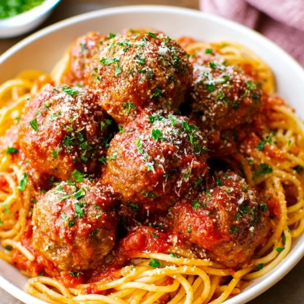 Oven-baked Italian meatballs served on a plate with sauce and herbs.