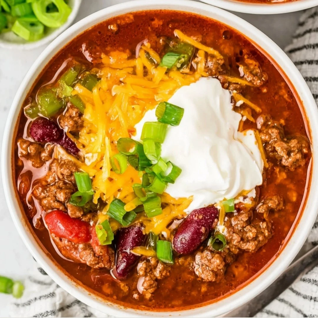 A warm bowl of simple beef and bean chili topped with cheese and herbs